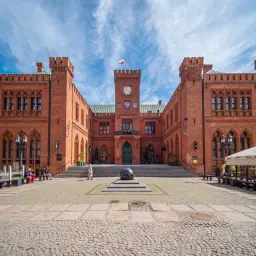 Imponujący ratusz na **rynku Kołobrzeg** z cegły, z wieżą zegarową i polską flagą.