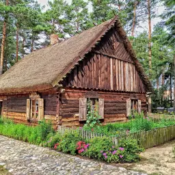 Drewniana chata z podlaskiej wsi, otoczona kwitnącym ogrodem i lasem. To piękny przykład architektury kurpiowskiej.
