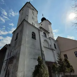 Biała, zabytkowa świątynia w Proszowicach pod błękitnym niebem z chmurami.