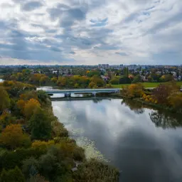 Jesioro Czerniakowskie w jesiennej szacie. Most przecina spokojną taflę wody, a wokół rozciąga się miasto i kolorowe drzewa.