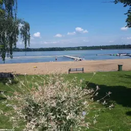 Słoneczny dzień nad jeziorem. Piękna plaża, zielona łąka i błękitne niebo tworzą idealne miejsce na wypoczynek.