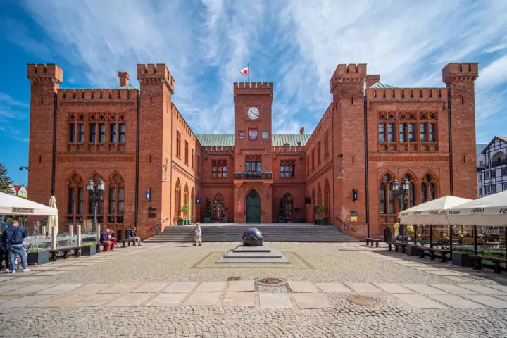 Imponujący ratusz na **rynku Kołobrzeg** z cegły, z wieżą zegarową i polską flagą.
