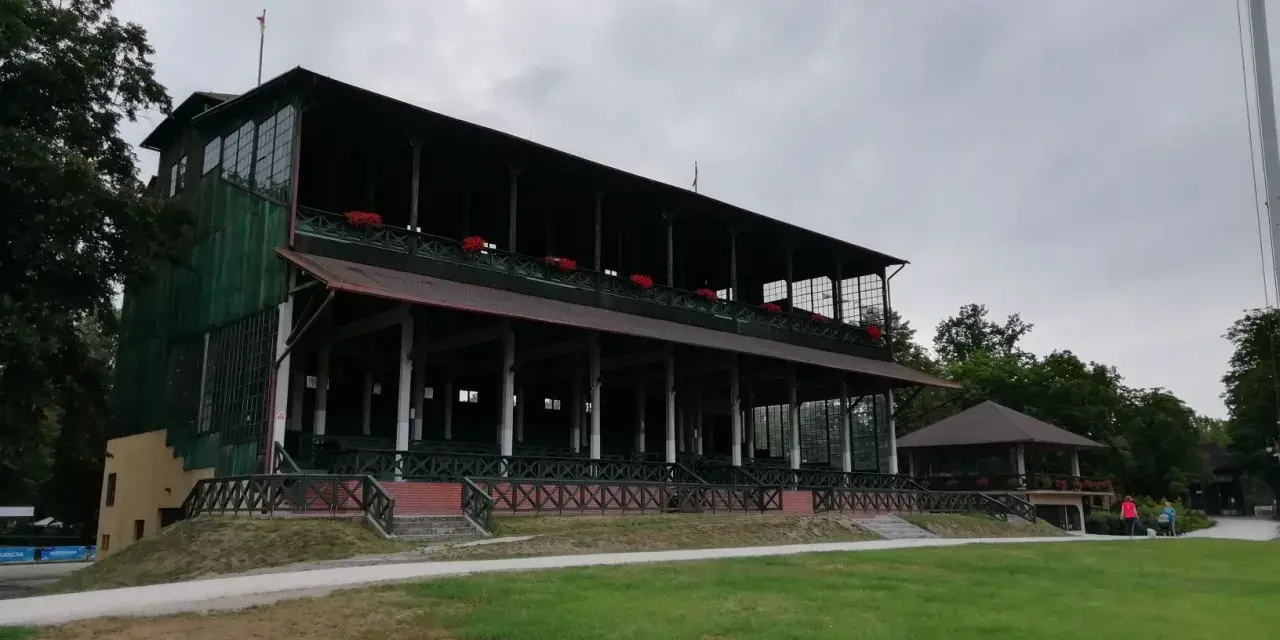 Stara, zielona trybuna w Kobierzycach z czerwonymi kwiatami na balustradzie.